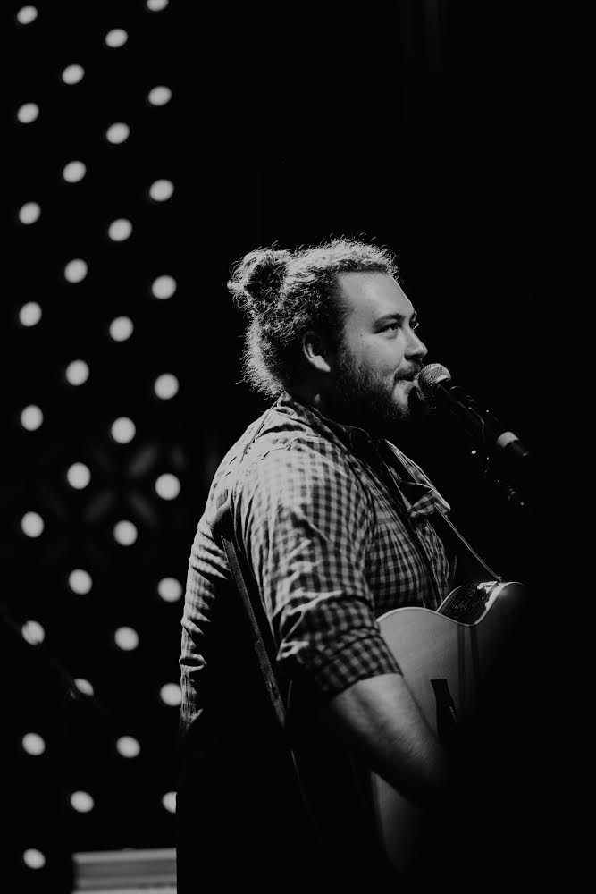 Singer-songwriter Graham DeFranco holding an acoustic guitar in a high-contrast black-and-white portrait